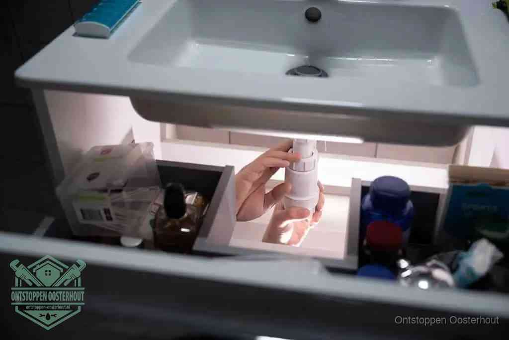 Een pompfles met zeep boven een wastafel, de heet water en afwasmiddel-methode om een vetprop in de afvoer los te maken in Oosterhout