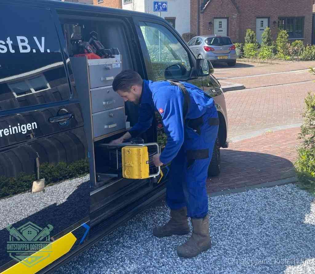 Een monteur pakt buiten op de oprit gereedschap uit de bedrijfsbus, het moment om een professional in te schakelen voor een verstopte afvoer in Oosterhout