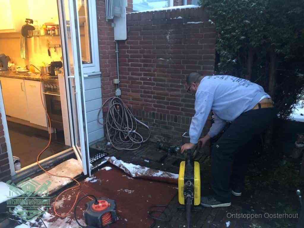 Een monteur werkt buiten bij een open riool-/grondput met een elektrische ontstoppingsmachine om een verborgen afvoerprobleem op te sporen in Oosterhout