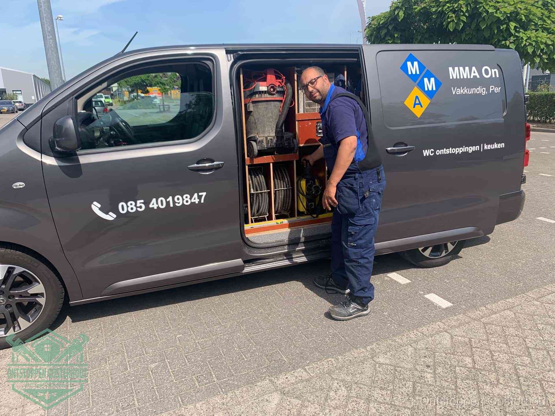 Een monteur bij de open schuifdeur van zijn bedrijfsbus op een parkeerplaats, klaar om de oorzaak van terugkerende afvoerverstoppingen aan te pakken in Oosterhout
