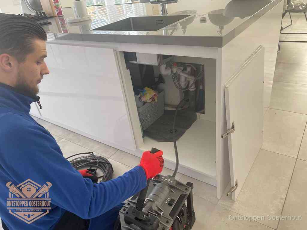 Monteur ontstopt met een veermachine een verstopte afvoer onder de gootsteen in Oosterhout