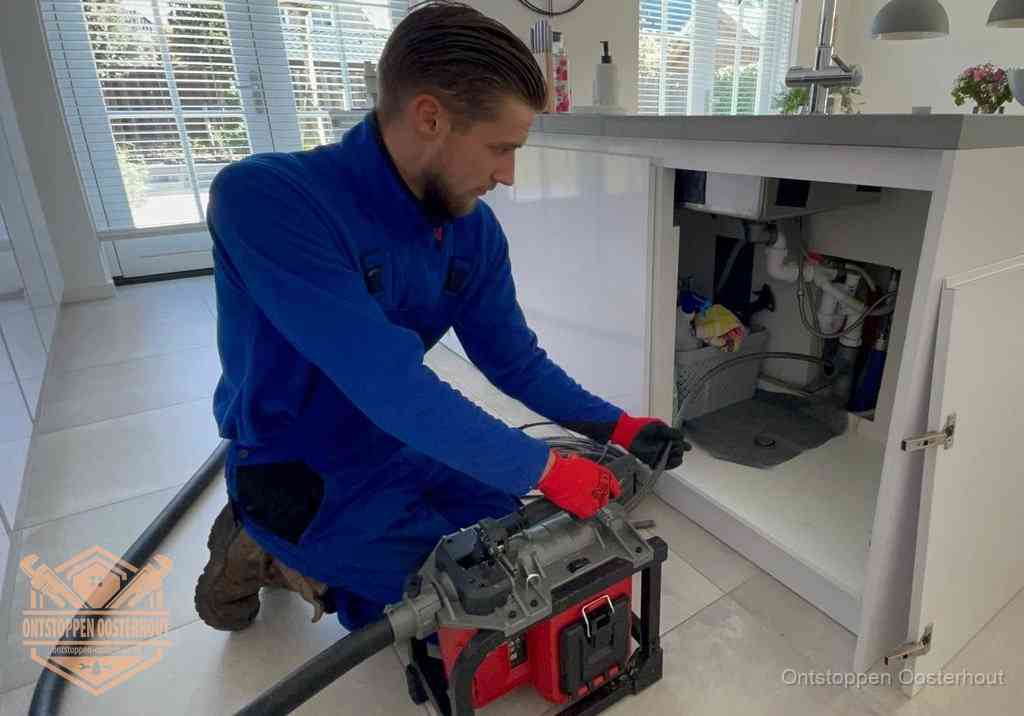 Een monteur voert een professionele elektrische ontstoppingsmachine in de afvoer onder de spoelbak tijdens het gootsteen ontstoppen in Oosterhout